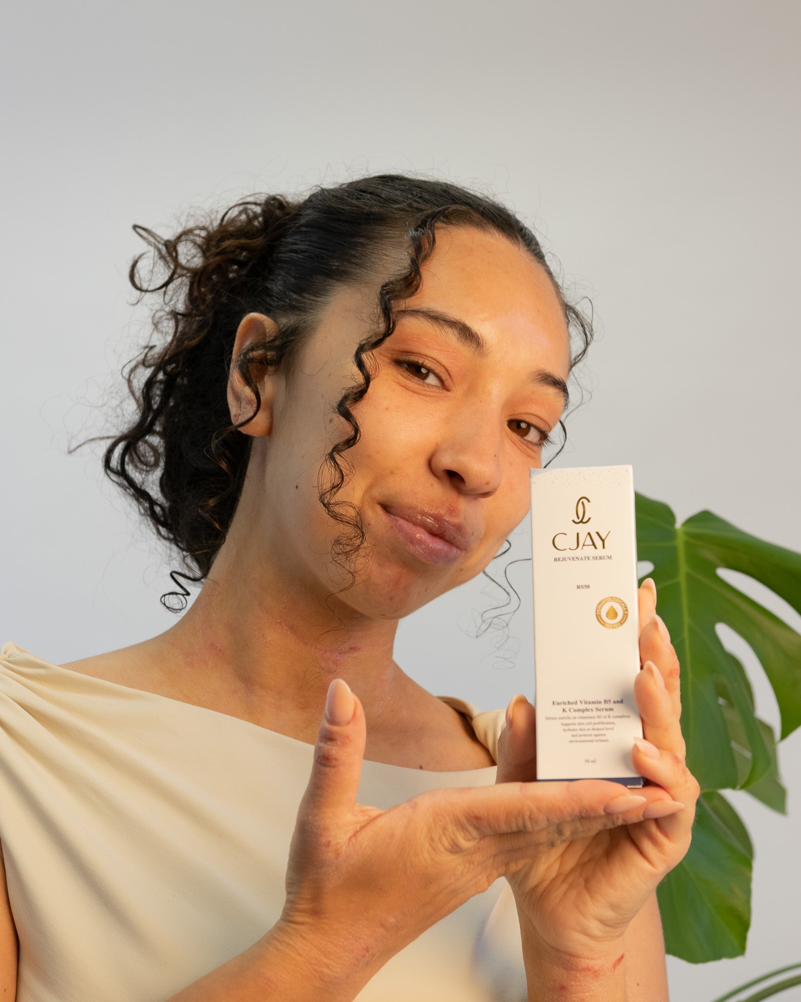 Woman holding a CJAY product against a neutral background with a plant.